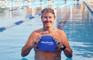 A man stands in a swimming pool lane holding a blue swimming cap
