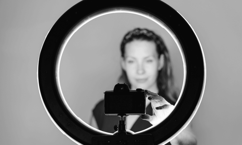 A woman stands in front of a ring light and camera